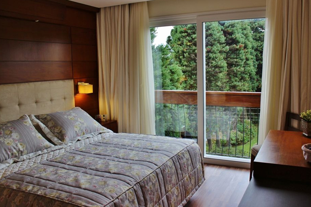 imagem do quarto com uma cama de casal e uma sacada com vista para a floresta.
