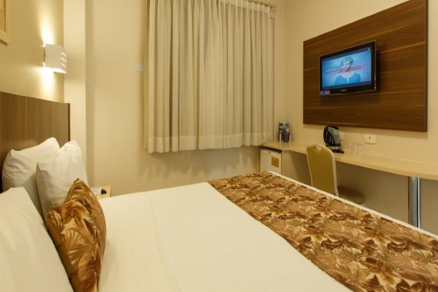 imagem do quarto contendo uma cama de casale uma tv, uma cadeira e mesa.