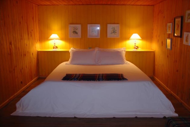 imagem de um quarto de madeira cama de casal com duas luminárias cada uma do lado da cama.