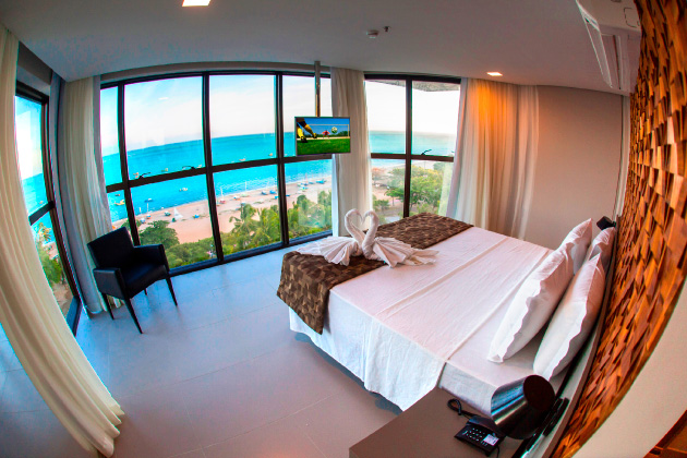 imagem do quarto com uma cama de casal com vista para o mar e uma tv a frente.
