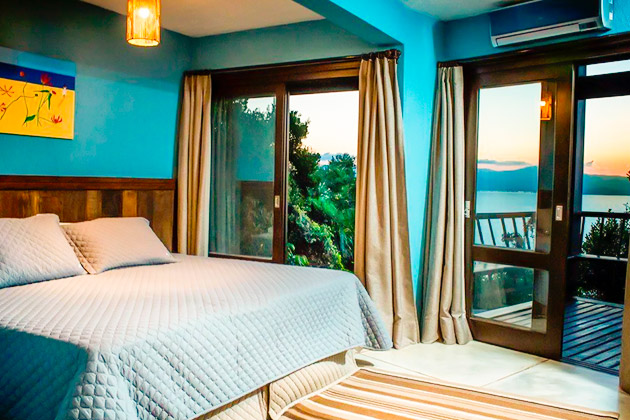 imagem do quarto com vista para o mar, sacada com deck de madeira e as paredes com cor azul