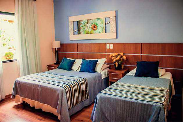 imagem do quarto com uma cama de casal e uma cama de solteiro, a parede atrás das camas é em azul.