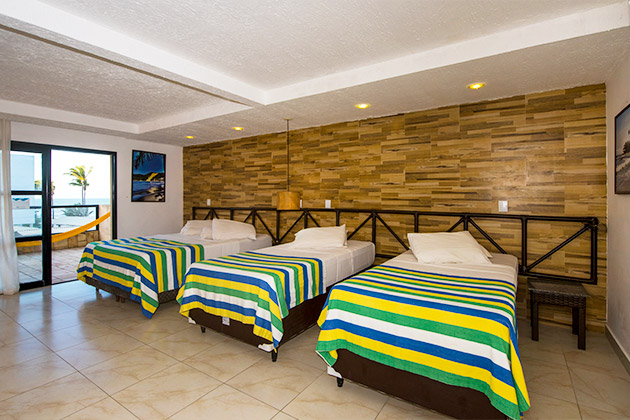 imagem do quarto com duas camas de solteiro e uma cama de casal. Varanda com vista para o mar.