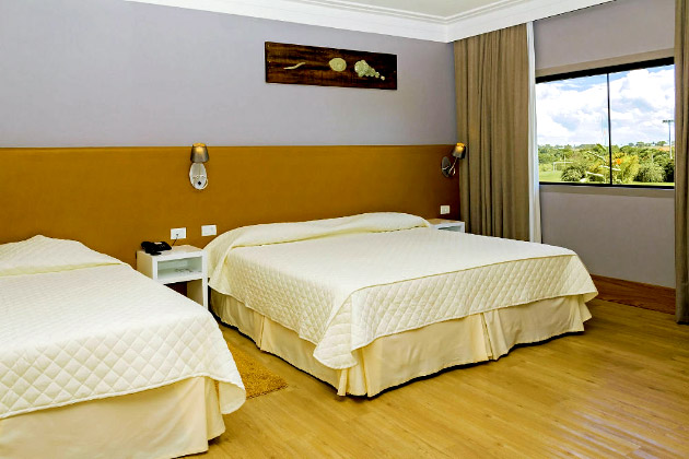 imagem de duas camas de casais, piso de madeira e uma vista para o campo.